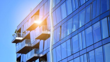 Modern cam bina ve yükselen güneş. Parlak güneşli bir günde mavi gökyüzünde güneş ışınlarıyla cam cephe. Ekonomi, finans, iş faaliyeti kavramı.  