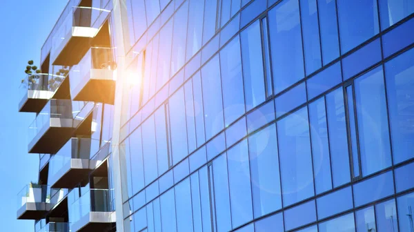 Modern glass building and rising sun. Glass facade on a bright sunny day with sunbeams in the blue sky. Economy, finances, business activity concept.