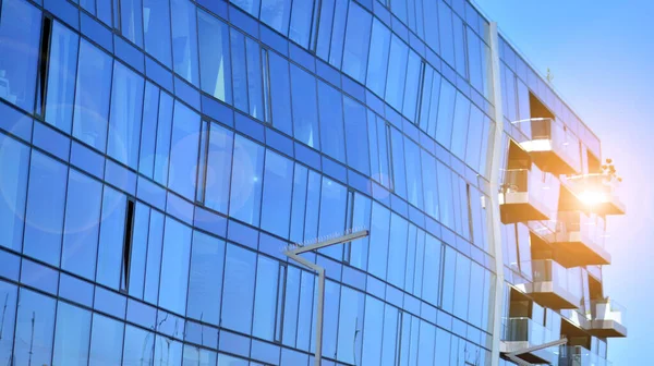 Modern glass building and rising sun. Glass facade on a bright sunny day with sunbeams in the blue sky. Economy, finances, business activity concept.