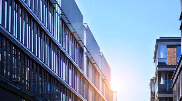 Modern glass building and rising sun. Glass facade on a bright sunny day with sunbeams in the blue sky. Economy, finances, business activity concept.