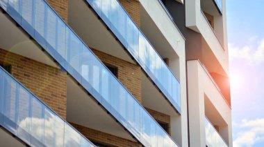 Mavi gökyüzü olan güneşli bir günde modern apartman binaları. Modern bir apartmanın ön cephesi. Güneş ışığıyla cam yüzey.