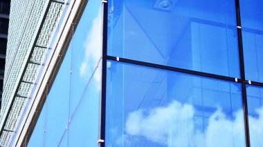 Mavi gökyüzü ve bulutlar modern ofis binasının camlarına yansıyor. Modern cam cephe. 