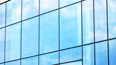 Mavi gökyüzü ve bulutlar modern ofis binasının camlarına yansıyor. Modern cam cephe. 
