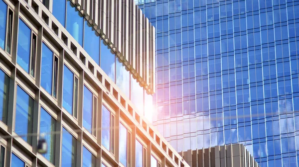 Facade texture of a glass mirrored office building. Fragment of the facade. Bottom view of modern skyscrapers in business district in evening light at sunset with lens flare filter effect.