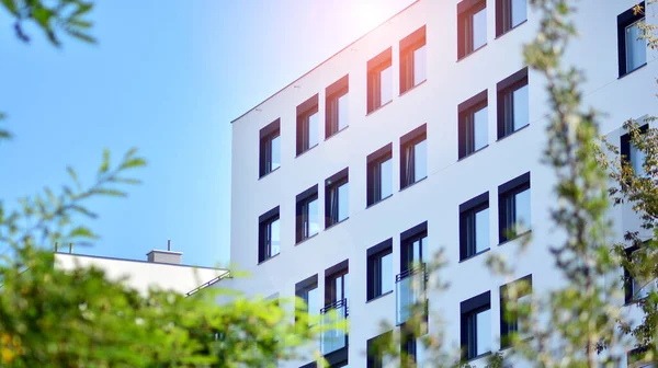 Ecological housing architecture. A modern residential building in the vicinity of trees. Ecology and green living in city, urban environment concept. Modern apartment building and green trees.