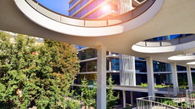 Modern luxury office building.The structure features a glass and concrete walls, showcasing contemporary architecture. The green surroundings of office buildings. Trees and shrubs in the city.