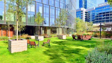Modern luxury office building.The structure features a glass and concrete walls, showcasing contemporary architecture. The green surroundings of office buildings. Trees and shrubs in the city.