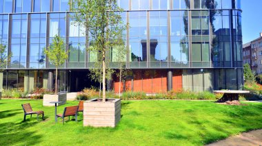 Modern luxury office building.The structure features a glass and concrete walls, showcasing contemporary architecture. The green surroundings of office buildings. Trees and shrubs in the city.