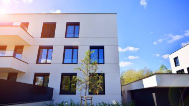 Balkonları ve yeşillikleri olan modern bir apartman. Yapıda cam bir duvar ve önde çağdaş mimari sergilenen yemyeşil bitkiler yer alıyor..