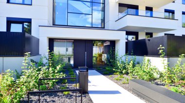 Balkonları ve yeşillikleri olan modern bir apartman. Yapıda cam bir duvar ve önde çağdaş mimari sergilenen yemyeşil bitkiler yer alıyor..