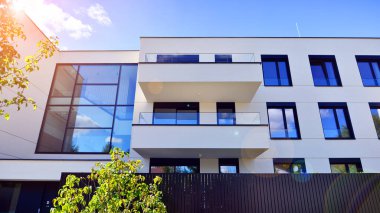 Balkonları ve yeşillikleri olan modern bir apartman. Yapıda cam bir duvar ve önde çağdaş mimari sergilenen yemyeşil bitkiler yer alıyor..