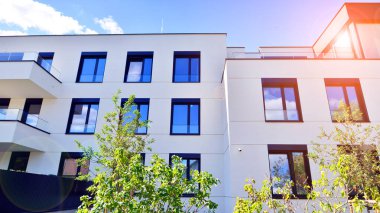 Balkonları ve yeşillikleri olan modern bir apartman. Yapıda cam bir duvar ve önde çağdaş mimari sergilenen yemyeşil bitkiler yer alıyor..