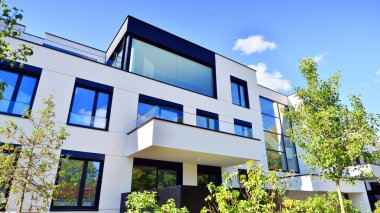 Balkonları ve yeşillikleri olan modern bir apartman. Yapıda cam bir duvar ve önde çağdaş mimari sergilenen yemyeşil bitkiler yer alıyor..