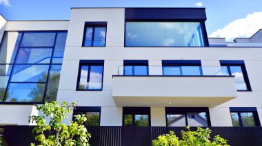 Balkonları ve yeşillikleri olan modern bir apartman. Yapıda cam bir duvar ve önde çağdaş mimari sergilenen yemyeşil bitkiler yer alıyor..