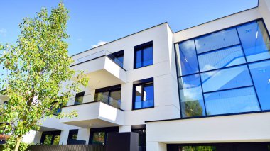 Balkonları ve yeşillikleri olan modern bir apartman. Yapıda cam bir duvar ve önde çağdaş mimari sergilenen yemyeşil bitkiler yer alıyor..