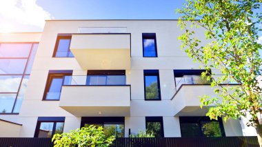 Balkonları ve yeşillikleri olan modern bir apartman. Yapıda cam bir duvar ve önde çağdaş mimari sergilenen yemyeşil bitkiler yer alıyor..