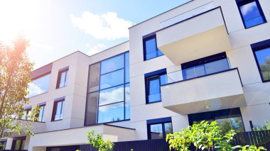 Balkonları ve yeşillikleri olan modern bir apartman. Yapıda cam bir duvar ve önde çağdaş mimari sergilenen yemyeşil bitkiler yer alıyor..