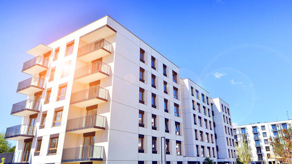 A residential building  by lush green trees and surrounded by  fresh vegetation on a clear sunny day. Modern architecture residential apartment building complex surrounded by greenery.
