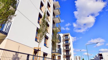 Bereketli yeşil ağaçlarla çevrili ve güneşli bir günde taze bitki örtüsüyle çevrili bir yerleşim yeri. Çağdaş mimari konut kompleksi yeşilliklerle çevrili.