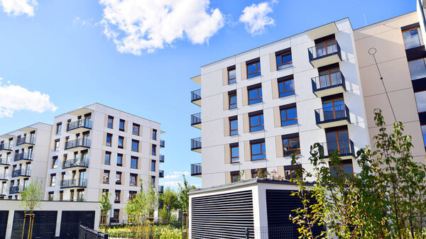A residential building  by lush green trees and surrounded by  fresh vegetation on a clear sunny day. Modern architecture residential apartment building complex surrounded by greenery.
