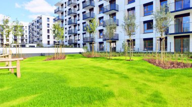 Bereketli yeşil ağaçlarla çevrili ve güneşli bir günde taze bitki örtüsüyle çevrili bir yerleşim yeri. Çağdaş mimari konut kompleksi yeşilliklerle çevrili.