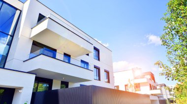 Balkonları ve yeşillikleri olan modern bir apartman. Yapıda cam bir duvar ve önde çağdaş mimari sergilenen yemyeşil bitkiler yer alıyor..