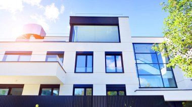 Balkonları ve yeşillikleri olan modern bir apartman. Yapıda cam bir duvar ve önde çağdaş mimari sergilenen yemyeşil bitkiler yer alıyor..