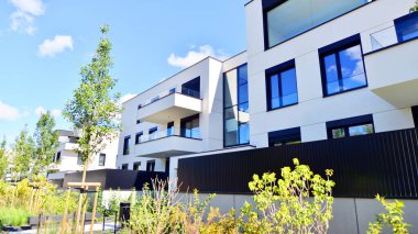 Balkonları ve yeşillikleri olan modern bir apartman. Yapıda cam bir duvar ve önde çağdaş mimari sergilenen yemyeşil bitkiler yer alıyor..