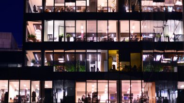 Şehir merkezindeki modern ofis binası gece aydınlandı. Modern bir cephenin mimari ızgarasına karşı yanan pencereler.