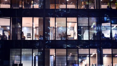 Şehir merkezindeki modern ofis binası gece aydınlandı. Modern bir cephenin mimari ızgarasına karşı yanan pencereler.