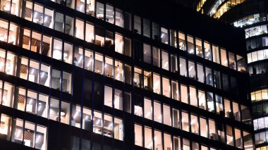 Şehir merkezindeki modern ofis binası gece aydınlandı. Modern bir cephenin mimari ızgarasına karşı yanan pencereler.