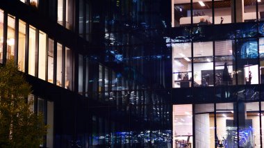 Şehir merkezindeki modern ofis binası gece aydınlandı. Modern bir cephenin mimari ızgarasına karşı yanan pencereler.