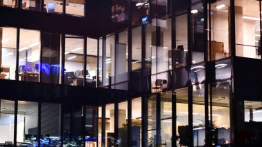 Şehir merkezindeki modern ofis binası gece aydınlandı. Modern bir cephenin mimari ızgarasına karşı yanan pencereler.