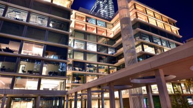 Şehir merkezindeki modern ofis binası gece aydınlandı. Modern bir cephenin mimari ızgarasına karşı yanan pencereler.