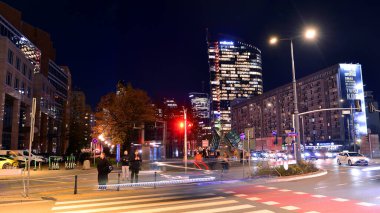 Varşova, Polonya. 4 Kasım 2025. Bulanık insanlar gecenin bir yarısı şehir merkezinde yaya geçidinde karşıdan karşıya geçiyorlar. Trafik ışıkları parlıyor ve etraflarında binalar yükseliyor. Yakınlarda geçen arabalar var..