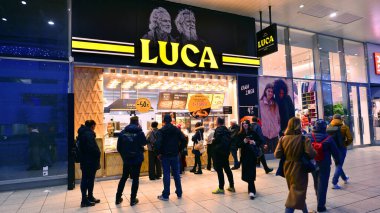 Varşova, Polonya. 4 Kasım 2025. İnsanlar hava karardıktan sonra büyük mağaza vitrinlerinin etrafında kaldırımlar boyunca yürürler. Lights caddesi ve etraflarında yükselen binalar. Yakınlarda geçen arabalar var..