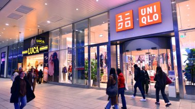 Varşova, Polonya. 4 Kasım 2025. İnsanlar hava karardıktan sonra büyük mağaza vitrinlerinin etrafında kaldırımlar boyunca yürürler. Lights caddesi ve etraflarında yükselen binalar. Yakınlarda geçen arabalar var..