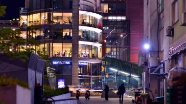 Varşova, Polonya. 4 Kasım 2025. İnsanlar geceleri kaldırımlar boyunca yürür. Lights caddesi ve etraflarında yükselen binalar. Yakınlarda geçen arabalar var..