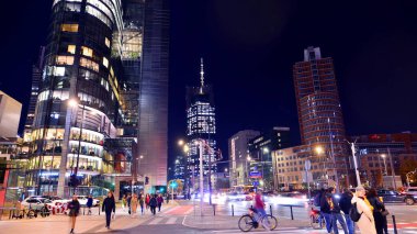 Varşova, Polonya. 4 Kasım 2025. Bulanık insanlar gecenin bir yarısı şehir merkezinde yaya geçidinde karşıdan karşıya geçiyorlar. Trafik ışıkları parlıyor ve etraflarında binalar yükseliyor. Yakınlarda geçen arabalar var..