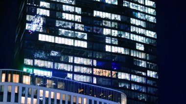 Şehir merkezindeki modern ofis binası gece aydınlandı. Aydınlatılmış pencereler modern bir cephenin mimari şebekesine karşı. Gece versiyonunda beton ve cam cephe.