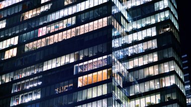 Şehir merkezindeki modern ofis binası gece aydınlandı. Aydınlatılmış pencereler modern bir cephenin mimari şebekesine karşı. Gece versiyonunda beton ve cam cephe.