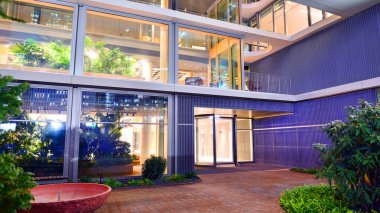 Şehir merkezindeki modern ofis binası gece aydınlandı. Aydınlatılmış pencereler modern bir cephenin mimari şebekesine karşı. Gece versiyonunda beton ve cam cephe.