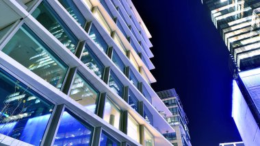 Şehir merkezindeki modern ofis binası gece aydınlandı. Aydınlatılmış pencereler modern bir cephenin mimari şebekesine karşı. Gece versiyonunda beton ve cam cephe.