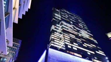 Şehir merkezindeki modern ofis binası gece aydınlandı. Aydınlatılmış pencereler modern bir cephenin mimari şebekesine karşı. Gece versiyonunda beton ve cam cephe.