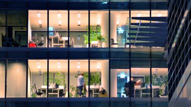 Şehir merkezindeki modern ofis binası gece aydınlandı. Aydınlatılmış pencereler modern bir cephenin mimari şebekesine karşı. Gece versiyonunda beton ve cam cephe.