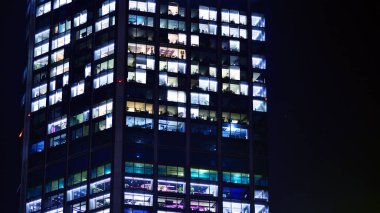 Şehir merkezindeki modern ofis binası gece aydınlandı. Aydınlatılmış pencereler modern bir cephenin mimari şebekesine karşı. Gece versiyonunda beton ve cam cephe.