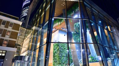 Modern ofis binasının zemin katında büyük cam pencereleri ve girişi olan gece görüşü. Sokak yansıması.