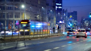 Varşova, Polonya. 21 Ocak 2026. Hava karardıktan sonra şehir hayatı. Gece yarısı şehir merkezinde caddeden geçen arabaların olduğu bir trafik. Işıklar ve binalar etraflarında yükseliyor..