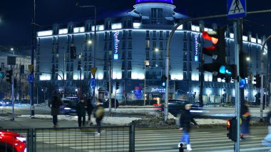 Varşova, Polonya. 21 Ocak 2026. İnsanlar gecenin bir yarısı şehir merkezinde yaya geçidinde karşıdan karşıya geçiyor. Trafik ışıkları parlıyor ve etraflarında binalar yükseliyor. Yakınlarda geçen arabalar var..