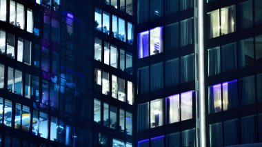 Modern ofis binasında geceleri büyük parlak pencereler, pencereler ışık saçıyor. Geceleri modern bir şirket binasının cam cephesinin bir parçası. Şehirde modern cam ofis.